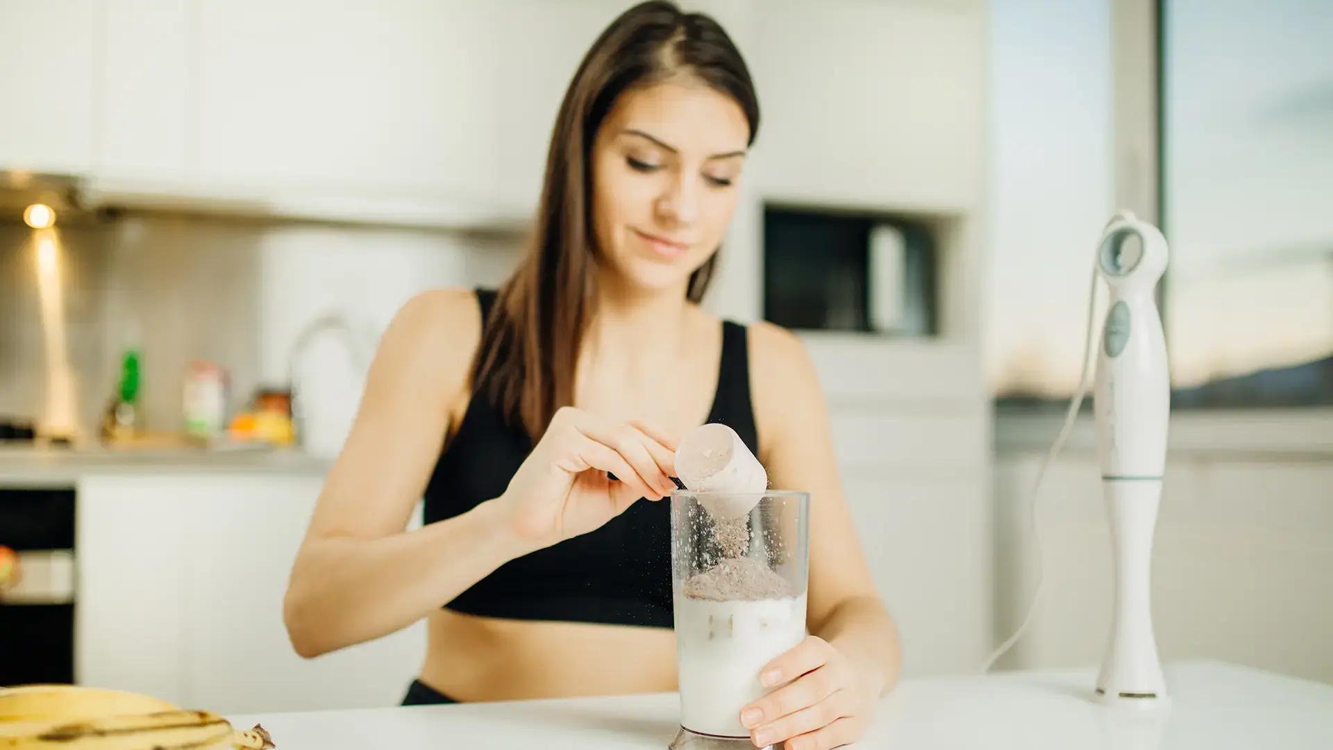 Woman with immersion blender making banana chocolate protein powder milkshake smoothie