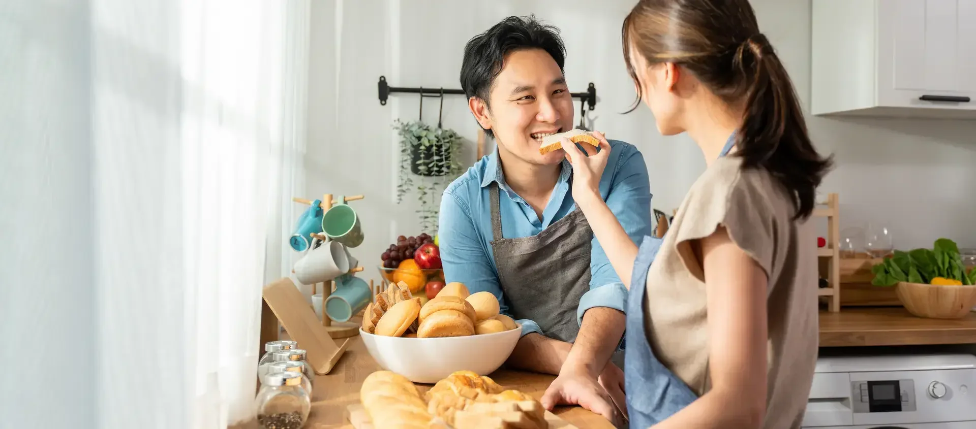 asian-young-female-holding-bread-and-giving-to-male-in-kitchen