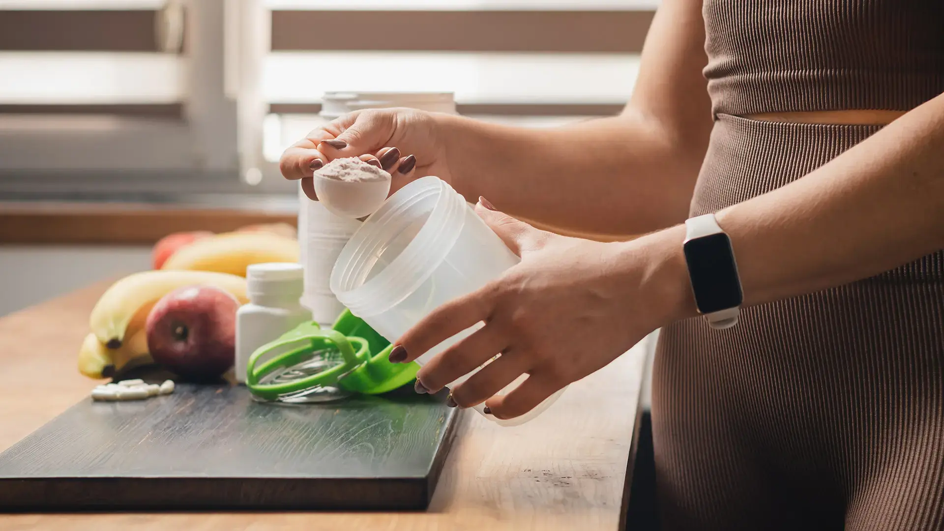 Athletic woman in sportswear with measuring spoon in her hand puts portion of whey protein powder