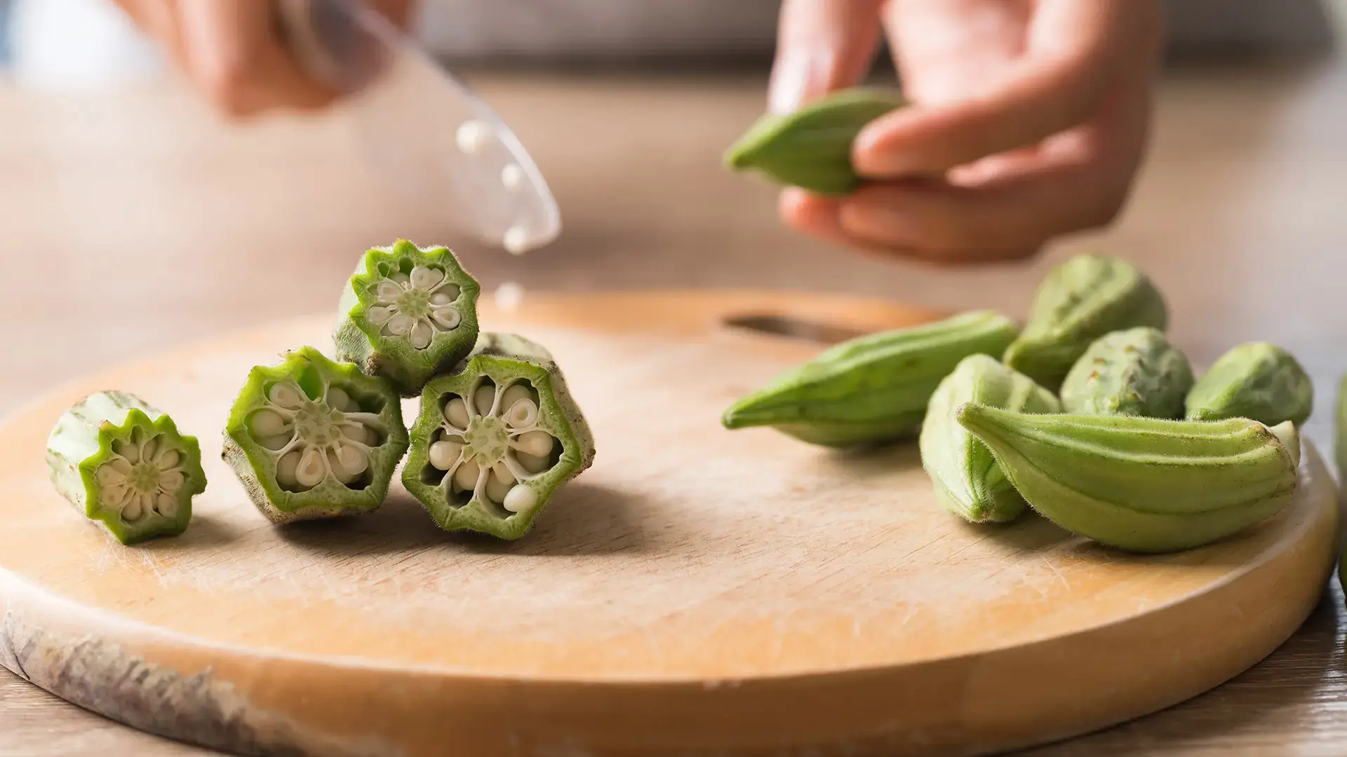 Hand holding knife and cutting green okra or ladies' fingers