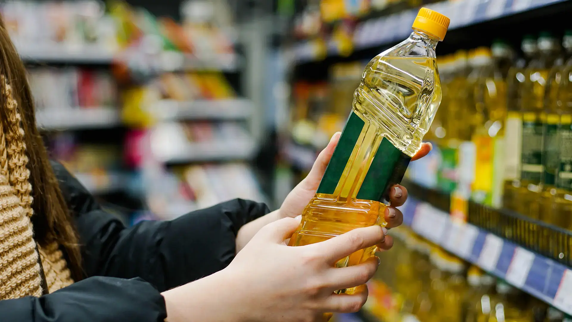 Woman-choosing-sunflower-oil-in-the-supermarket.-Close-up-of-hand-holding-bottle-of-oil-at-store
