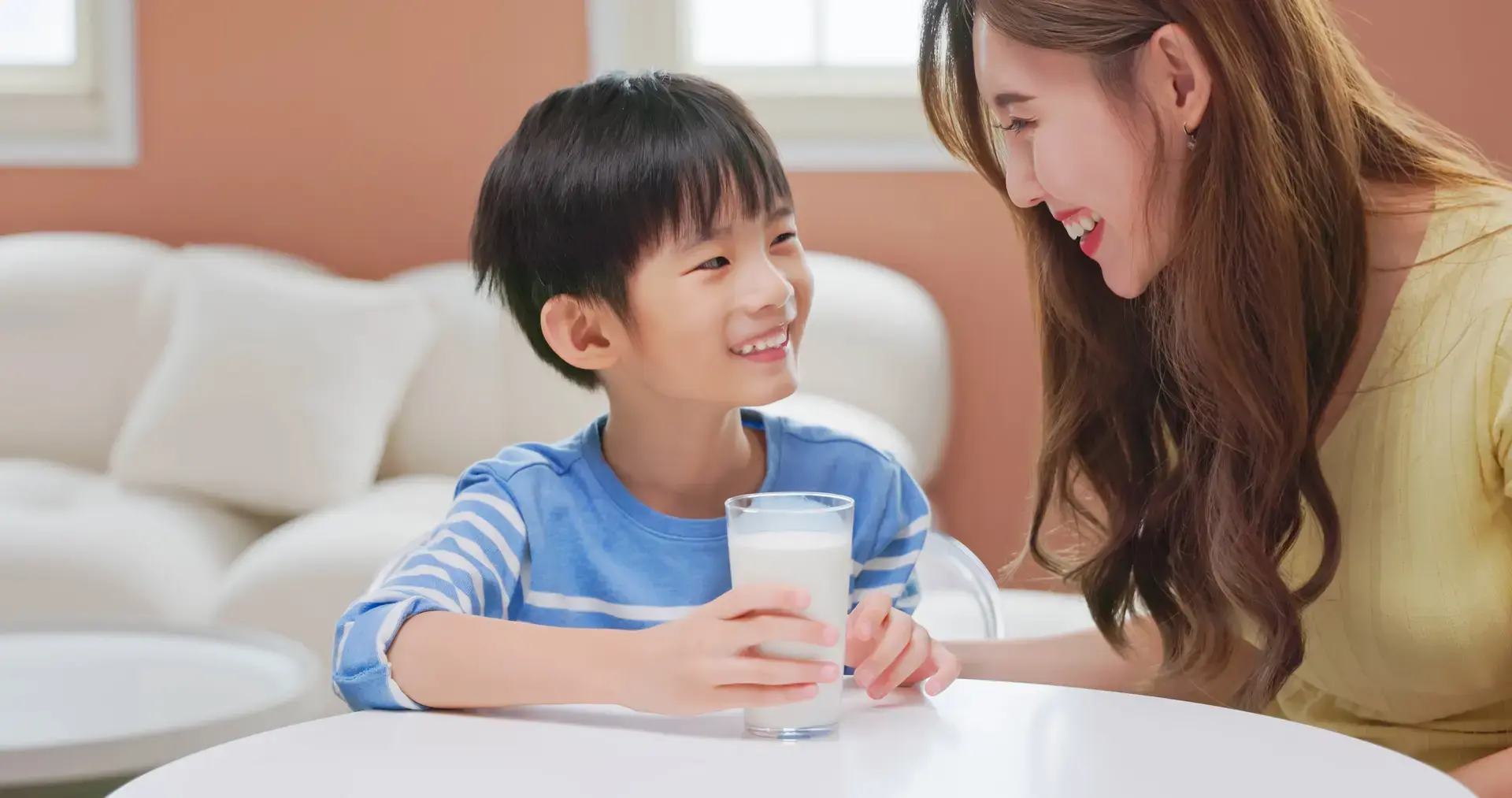 Asyanong batang lalaki na nakangiti sa kanyang nanay habang hawak ang isang basong gatas.