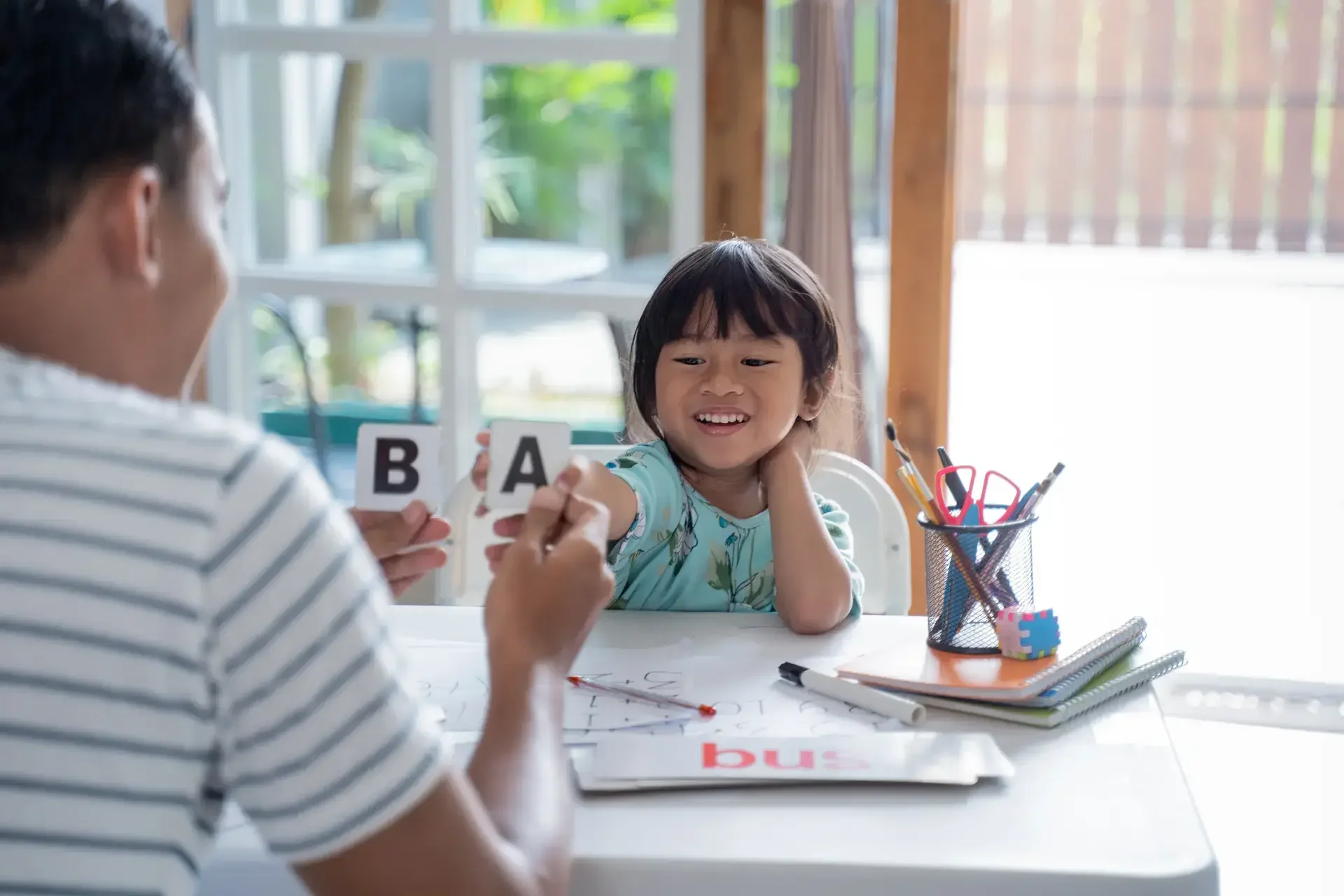 Asyanong tatay na tinuturuan ang kanyang batang anak na babae kung paano magbasa ng mga letra gamit ang flashcards.