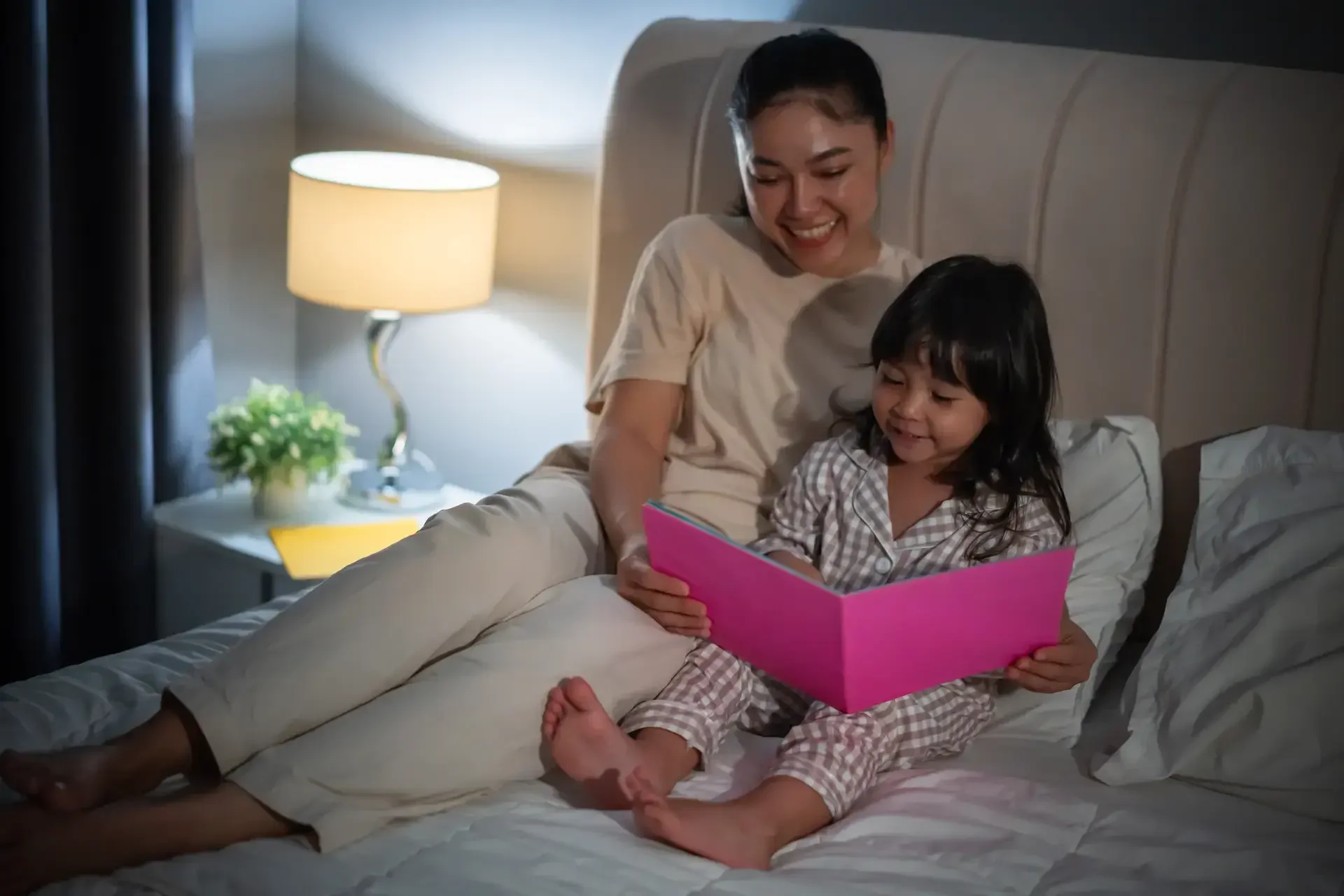 Batang natatawa habang binabasahan ng magulang ng bedtime story.