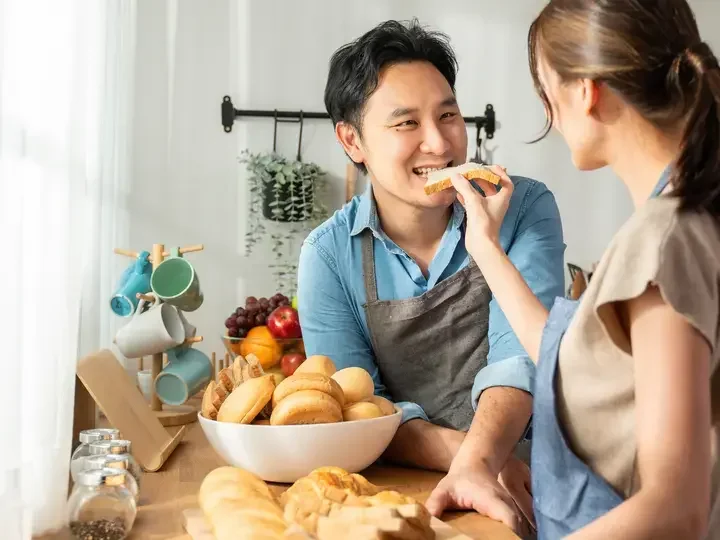 asian-young-female-holding-bread-and-giving-to-male-in-kitchen