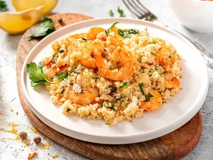 Couscous with shrimps, tomatoes, onions, and herbs in a white bowl close-up