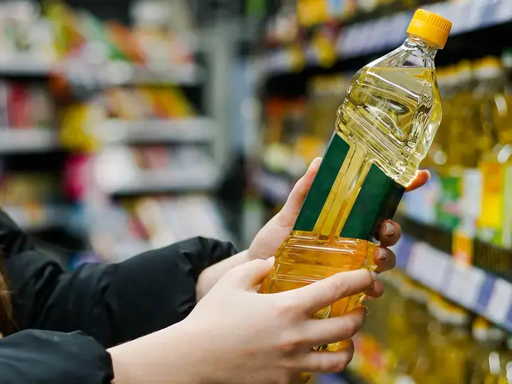 Woman-choosing-sunflower-oil-in-the-supermarket.-Close-up-of-hand-holding-bottle-of-oil-at-store