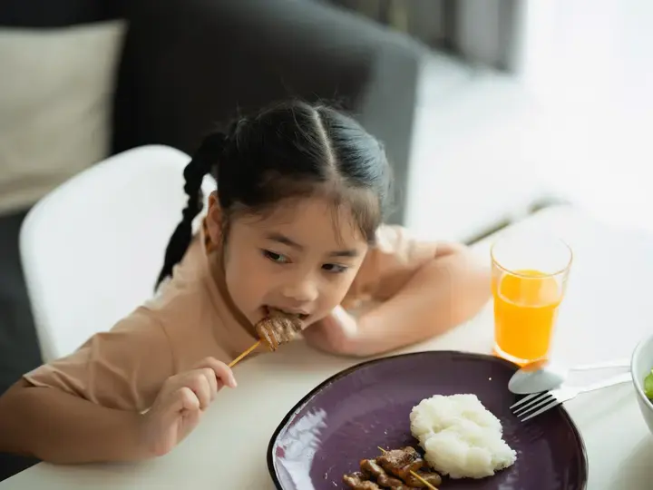 Batang babaeng Asyano na kumakain ng barbecue.