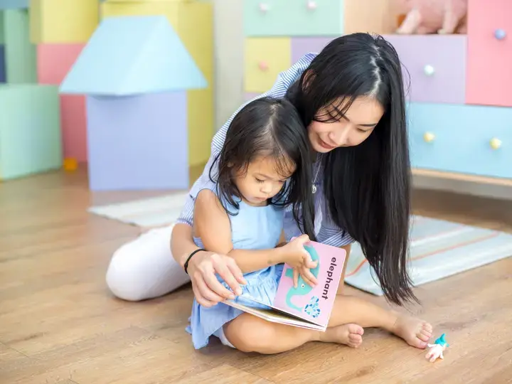 Asyanong nanay at batang anak na babae na nagbabasa ng libro.