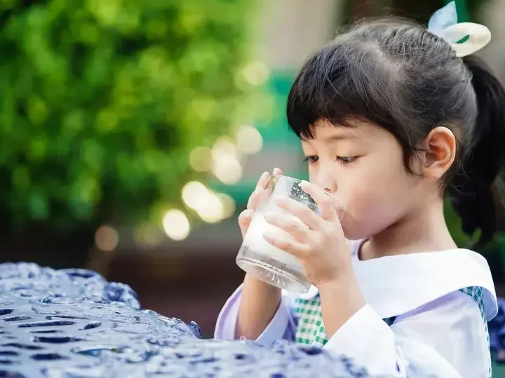 Asyanong batang babae na umiinom ng isang basong gatas.